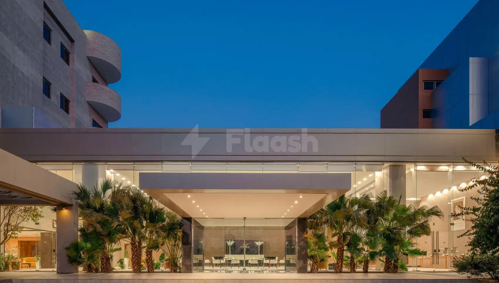 Lobby at Carlton Al Moaibed Hotel, Dammam, with glass walls and palm trees under evening sky