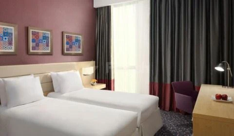 Guest room at Radisson Blu Residence, Dhahran, featuring twin bedsity beds and framed geometric art on pink walls
