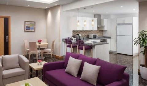 Living space at Radisson Blu Residence, Dhahran, featuring purple sofa and open kitchen with bar stools