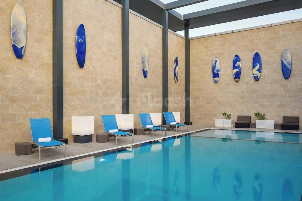 Indoor pool at Aloft Dhahran, Al Khobar, featuring blue surfboard art on stone walls and lounge chairs along