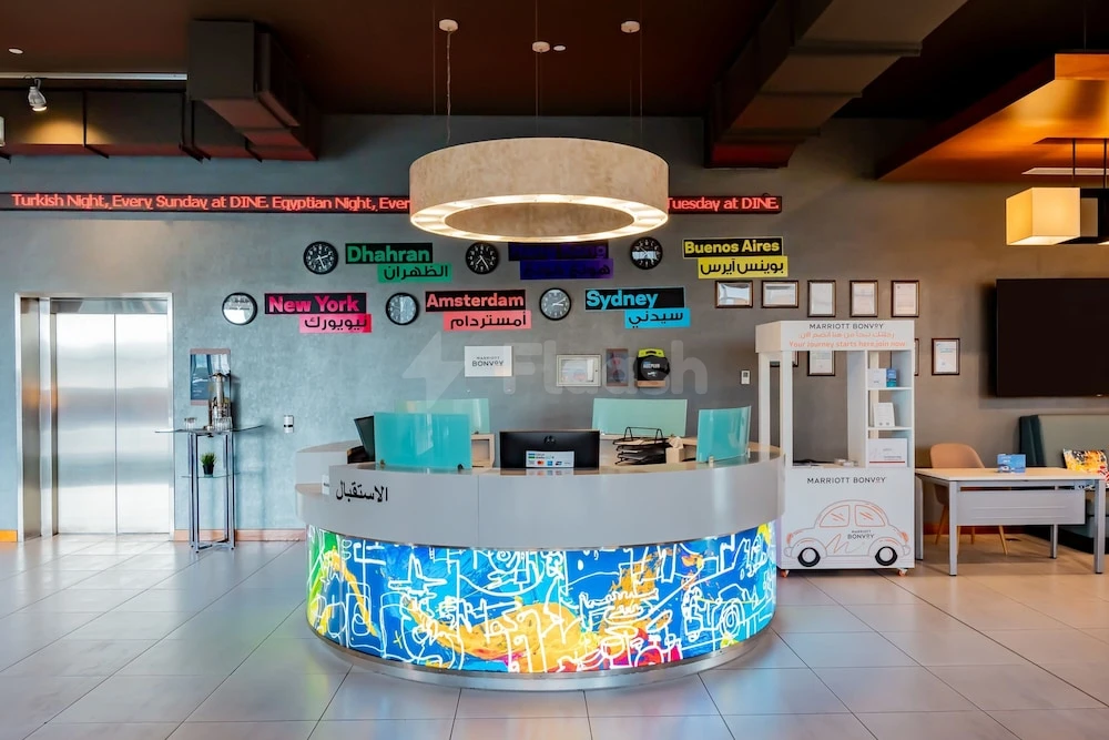 Reception area at Aloft Dhahran, Al Khobar, featuring a circular desk with vibrant city-themed mural and global time