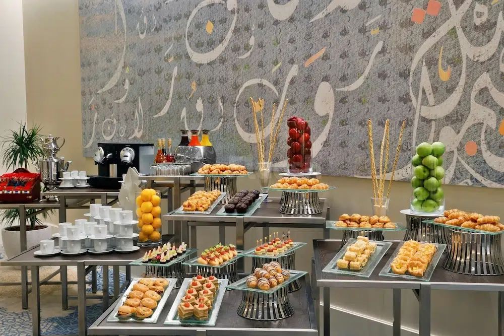 Buffet spread at Hilton Hotel & Convention Jabal, Makkah, featuring tiered trays of pastries and fruit arrangements