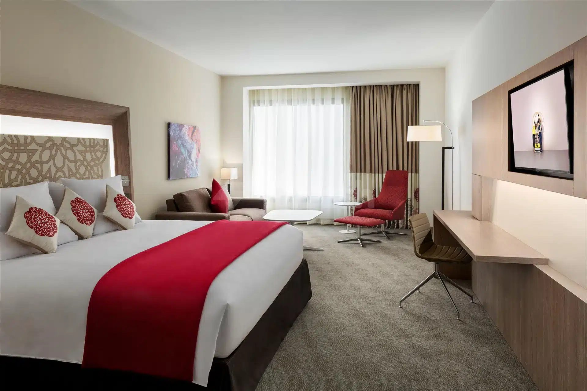 Guest room at Novotel JeddahPropTypes, Jeddah, featuring red accent pillows and a modern desk with mounted TV