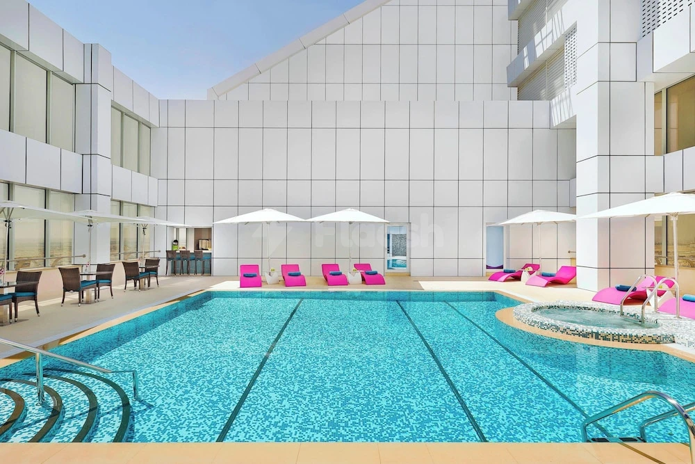 Outdoor pool at Courtyard by Marriott Riyadh Olaya, Riyadh, with bright pink loungers and white umbrellas beside modern