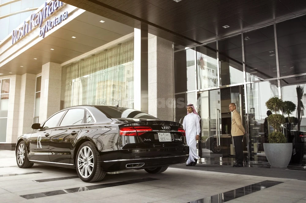 Grand entrance at Rosh Rayhaan by Rotana, Riyadh, with luxury sedan and uniformed staff at glass doors