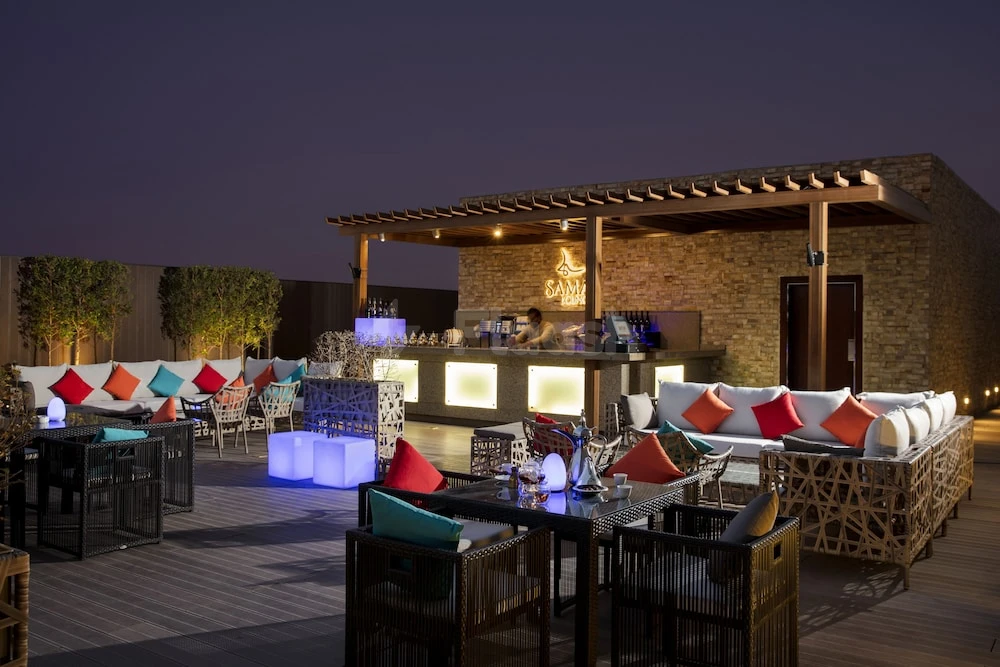 Rooftop lounge at Rosh Rayhaan By Rotana, Riyadh, featuring wicker sofas with colorful cushions and glowing blue cubes