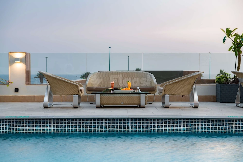 Rooftop pool at Radisson Blu Hotel, Jeddah Corniche, with lounge chairs and glass-topped table facing calm waters under