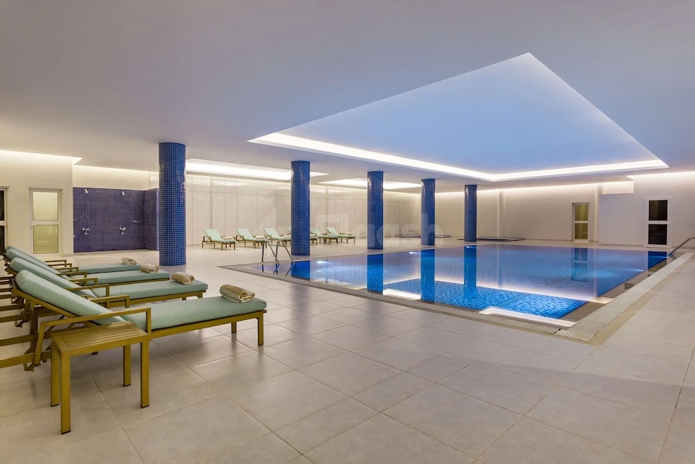 Indoor pool at Radisson Hotel Riyadh Airport, Riyadh, with turquoise lounge chairs and blue tiled columns