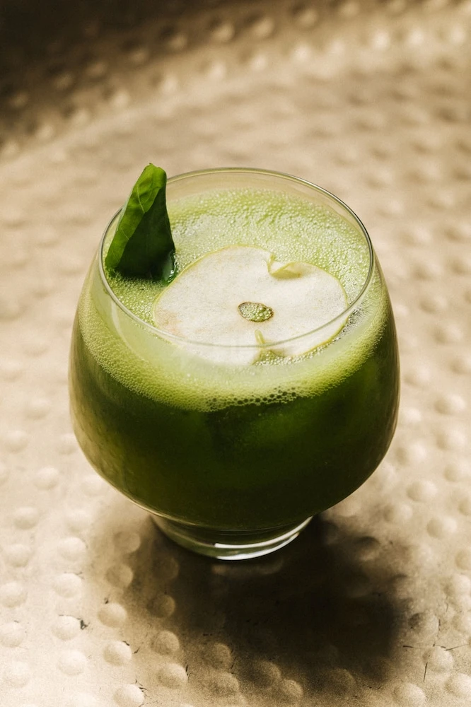 Green cocktail at Habitas AlUla, AlUla, garnished with basil leaf on textured metallic surface