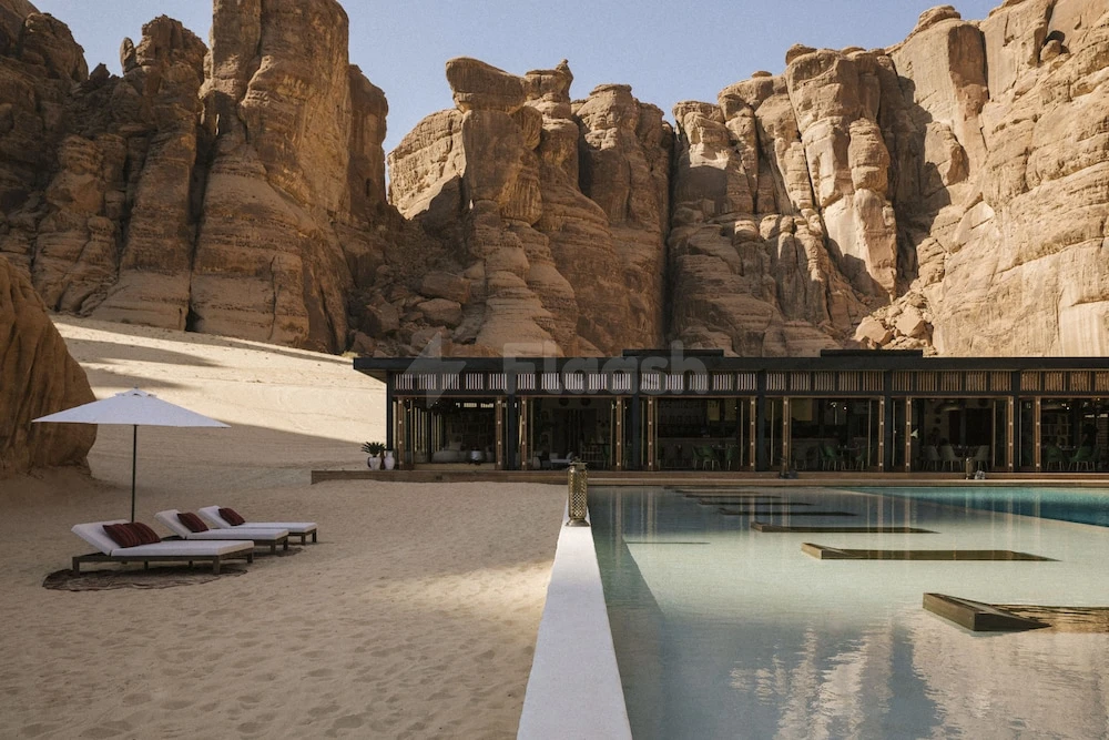 Infinity pool at Habitas AlUla, AlUla, framed by towering sandstone cliffs and sunlit lounge chairs on desert sand
