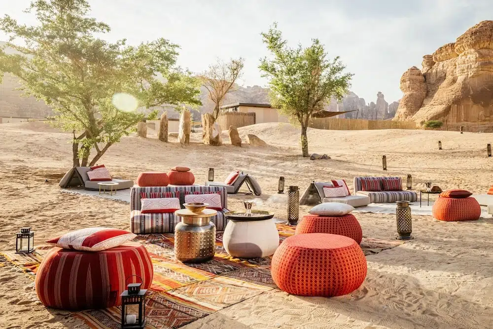 Outdoor lounge at Habitas AlUla, AlUla, with striped poufs and woven rugs under desert trees