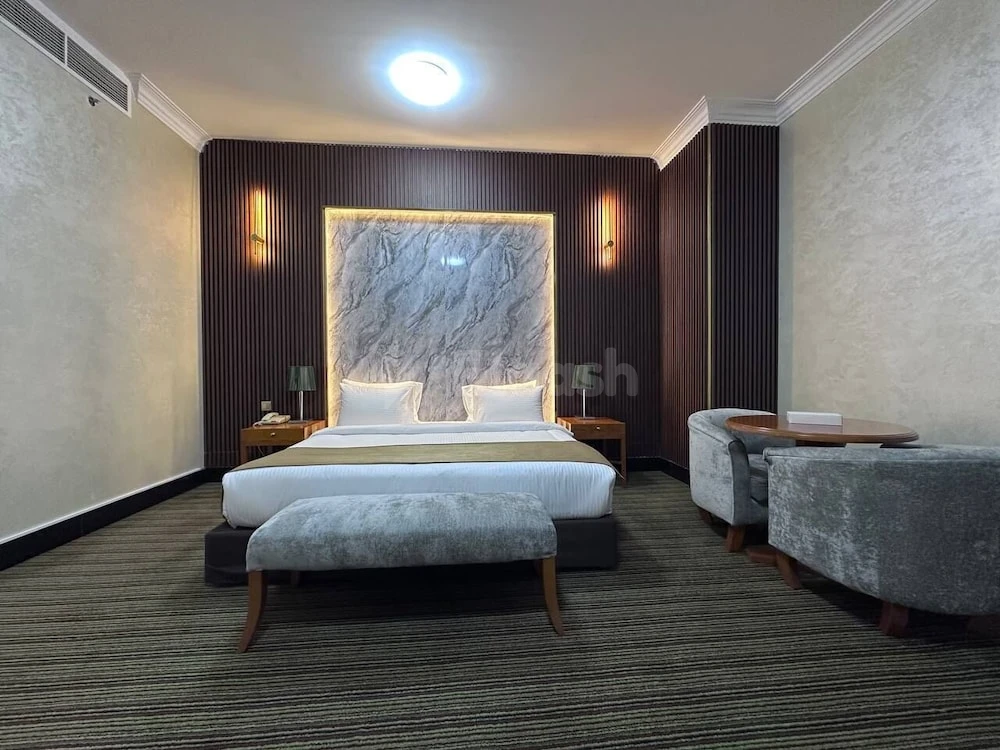 Guest room at Al Massa Hotel, Mecca, featuring a marble headboard bed and gray velvet seating