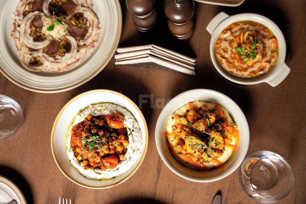 Dining table at Dar Tantora The House Hotel, AlUla, featuring colorful dishes on wooden surface with salt