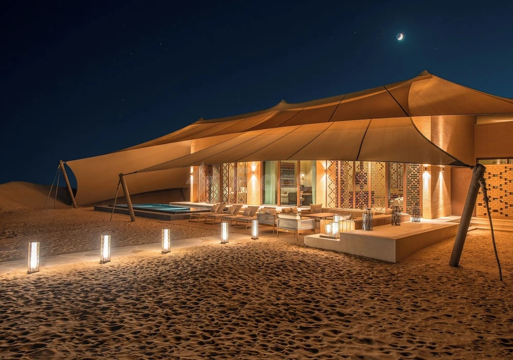 Desert lounge at Banyan Tree AlUla, AlUla, under moonlit sky with canopy tent and glowing lanterns on sand
