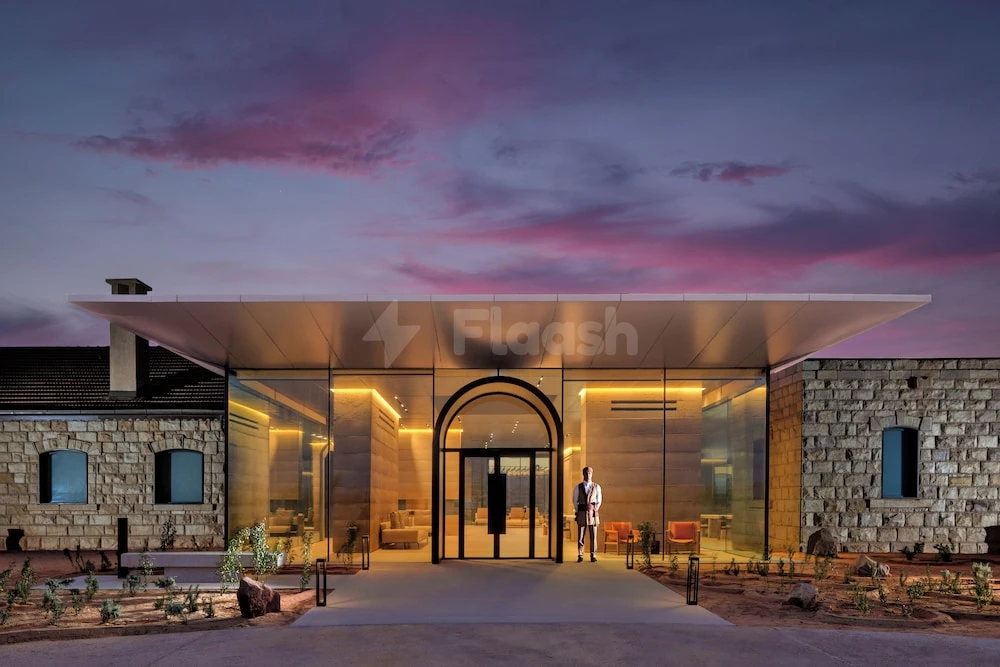 Glass entrance at The Chedi Hegra, AlUla, with arched doorway and stone-clad wings under a purple twilight sky