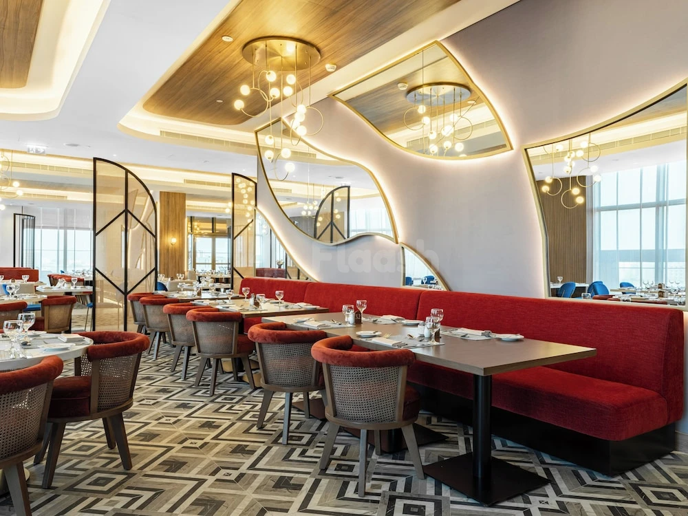 Dining area at voco Jeddah Gate, Jeddah, with red banquettes and geometric ceiling mirrors