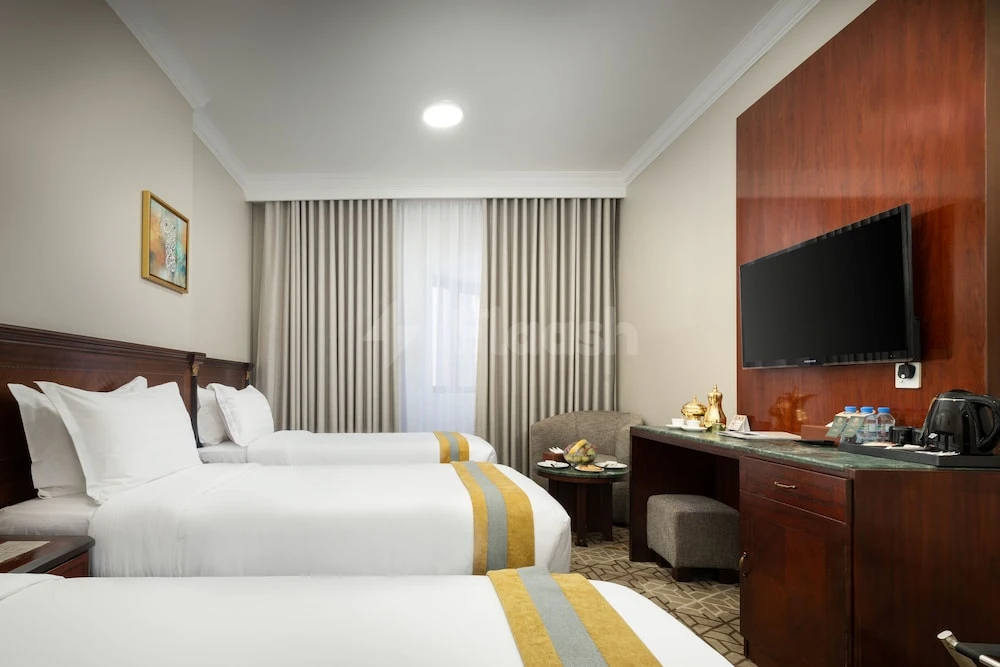 Guest room at Emaar Al Manar Hotel, Makkah, featuring twin beds with gold-trimmed linens and a wooden desk