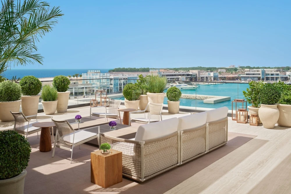 Rooftop terrace at The Jeddah EDITION, Jeddah, overlooking marina with white wicker furniture and potted greenery