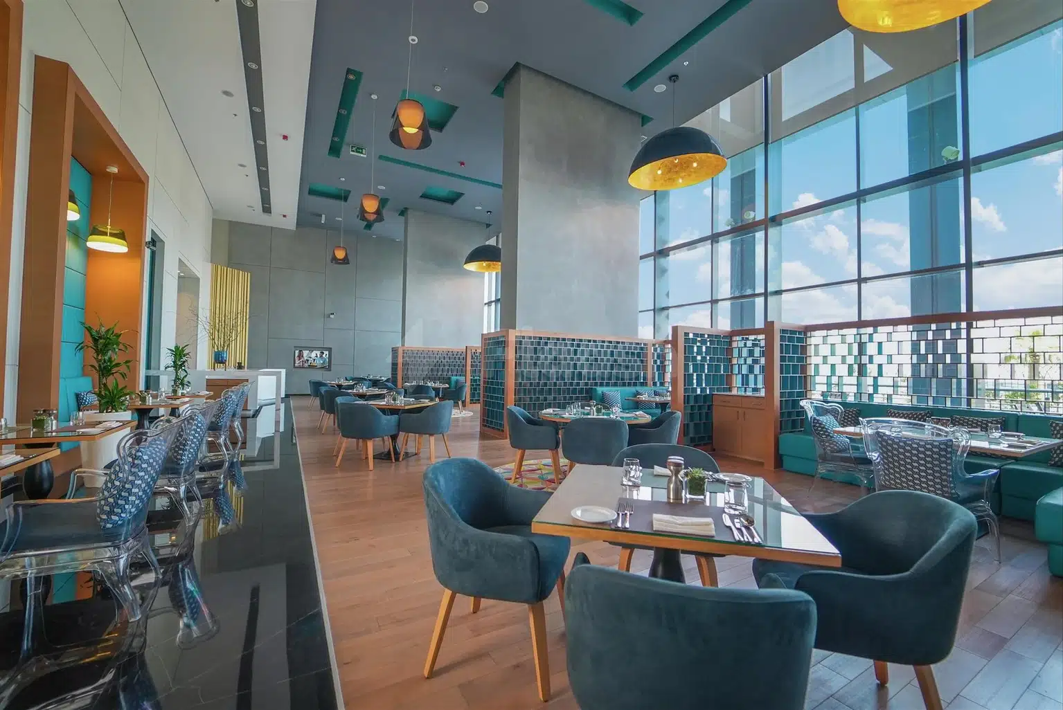 Dining area at Dana Rayhaan by Rotana, Dammam, with teal chairs and floor-to-ceiling windows overlooking cityscape