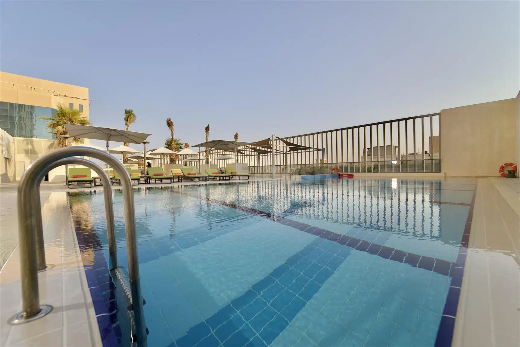 Outdoor swimming pool at Dana Rayhaan by Rotana, Dammam, with blue mosaic tiles and lounge chairs under