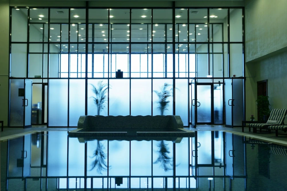 Indoor pool at Ramada Hotel & Suites by Wyndham Ajman, Ajman, with frosted glass walls and reflected palm trees