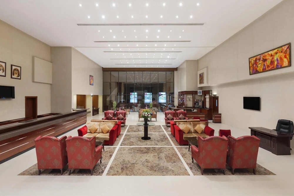 Lobby at Ramada Hotel & Suites by Wyndham Ajman, featuring red patterned armchairs and a large abstract painting