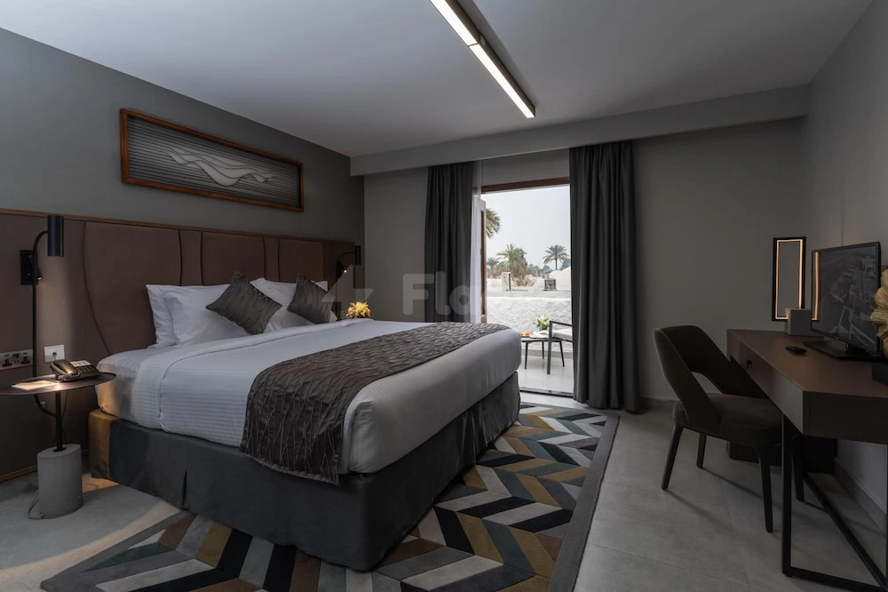 Guest room at Marbella Resort, Sharjah, featuring a geometric-patterned rug and sliding glass door to balcony