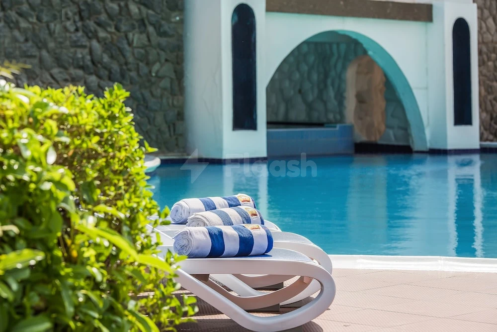 Poolside lounge area at Marbella Resort, Sharjah, with blue-tiled archway and striped towels on white chairs