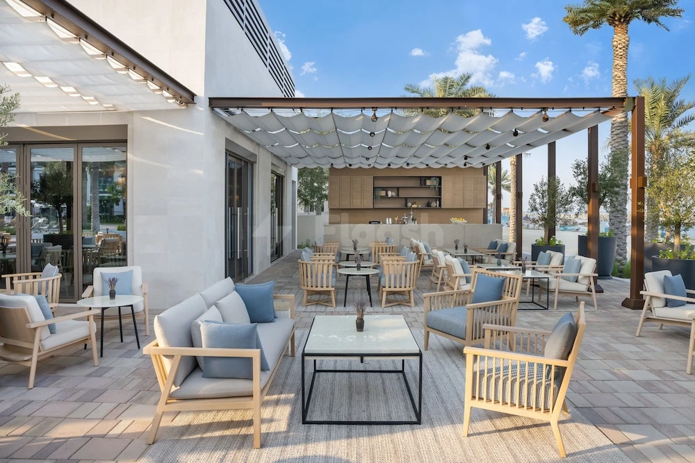 Outdoor lounge at Address Beach Resort Fujairah, Fujairah, with wooden furniture and palm trees under a canopy