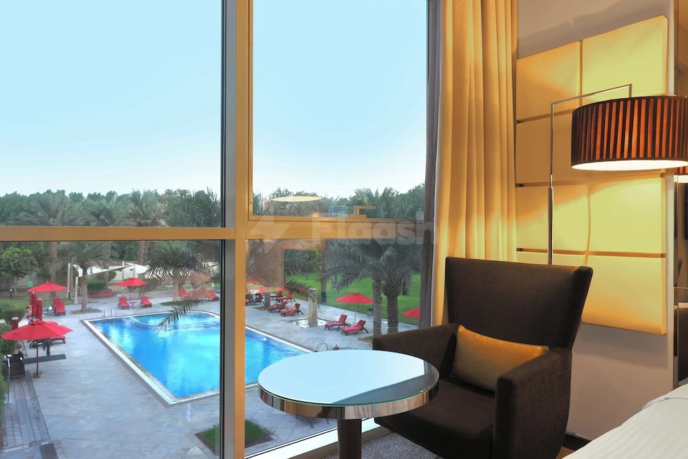 Lounge area at Centro Sharjah, Sharjah, with glass doors opening to a poolside terrace lined with red shaded