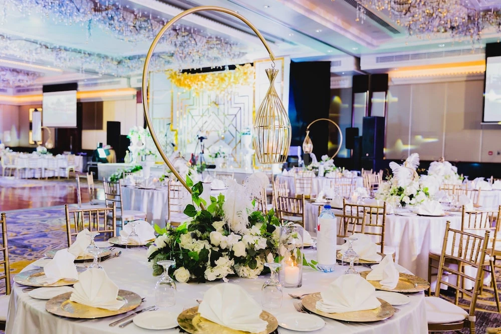 Banquet hall at Millennium Airport Hotel Dubai, set with white linens, gold chairs, and floral centerpieces under crystal