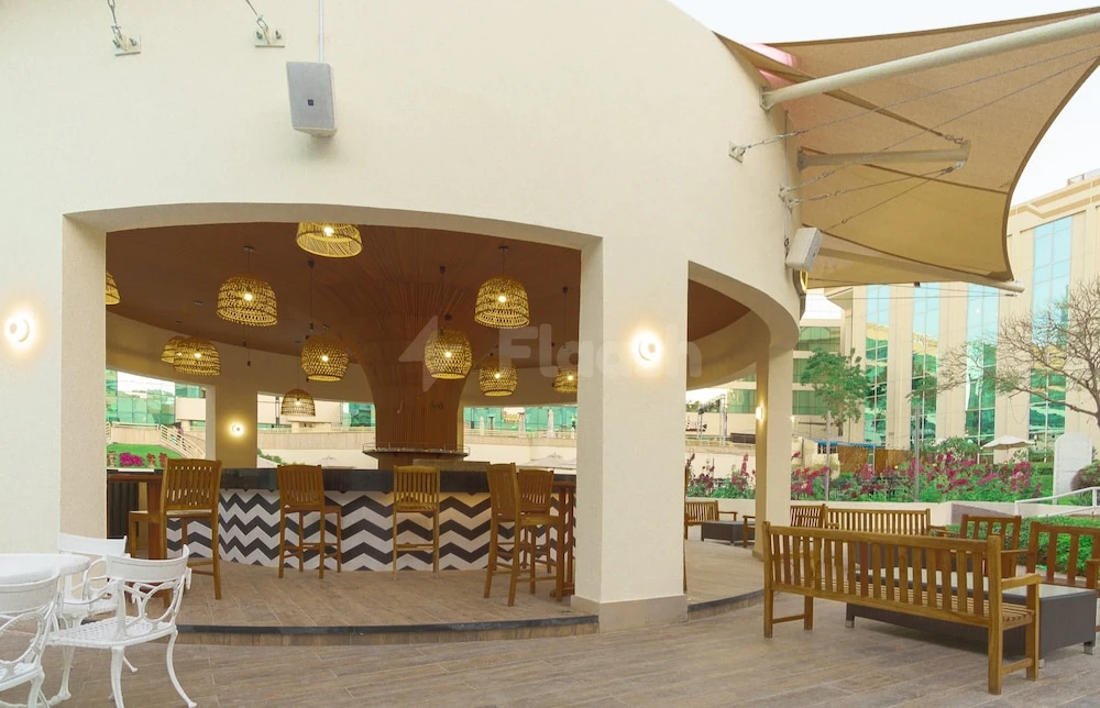 Outdoor lounge at Millennium Airport Hotel Dubai, featuring wooden furniture and woven pendant lights under a beige canopy
