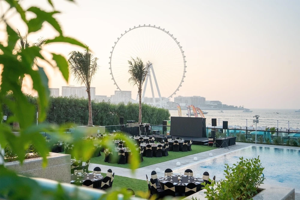 Poolside event space at Hilton Dubai Jumeirah, Dubai, with tables on grass near pool and Ain Dubai Ferris