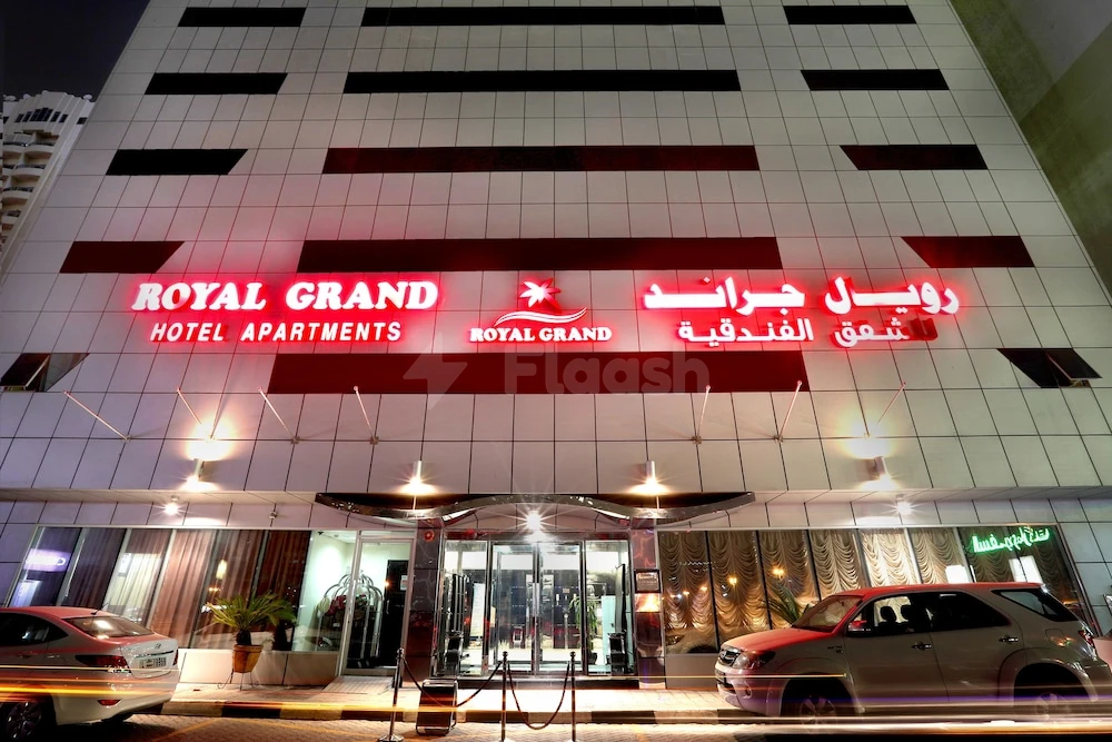 Facade of Royal Grand Hotel Apartments in Sharjah illuminated by red neon signage and glass entrance doors