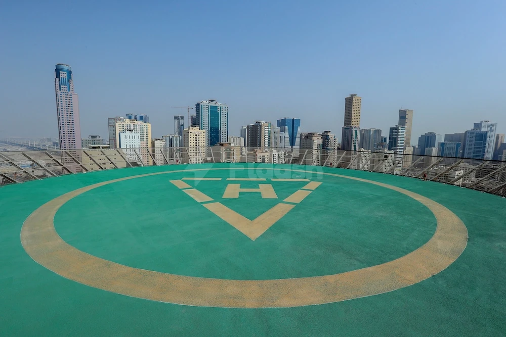 Helipad at Royal Grand Suite Hotel, Sharjah, with city skyline backdrop and green landing surface marked by white