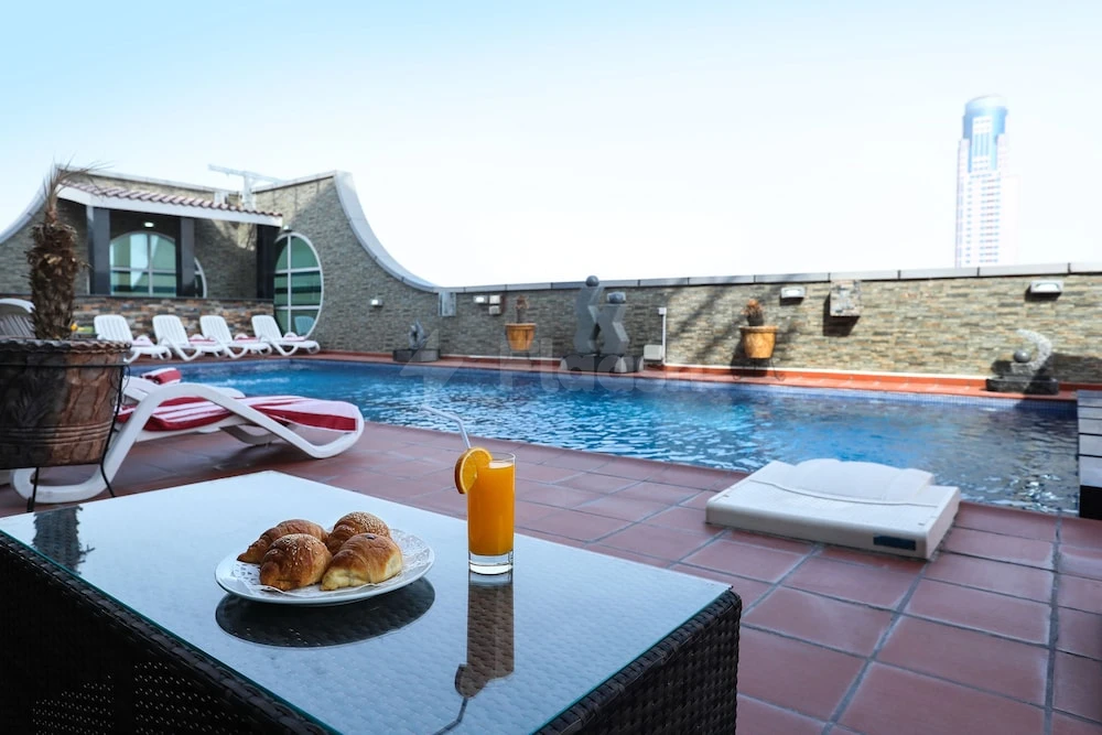 Rooftop pool at Royal Grand Suite Hotel, Sharjah, with breakfast spread and city skyline view