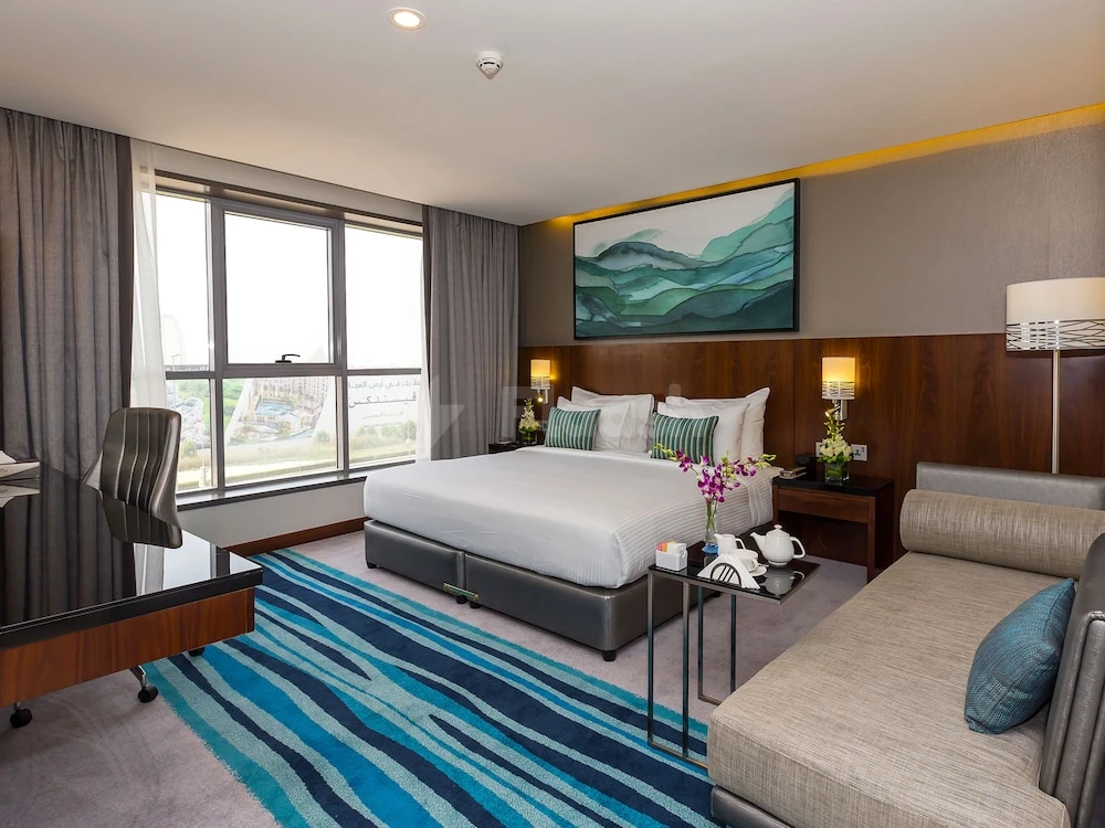 Guest room at Flora Al Barsha Hotel, Dubai, featuring a blue striped rug and abstract mountain artwork