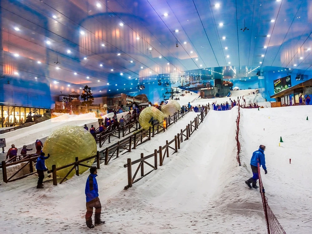 Indoor ski slope at Flora Al Barsha Hotel, Dubai, with snow-covered terrain and zorb balls under illuminated blue