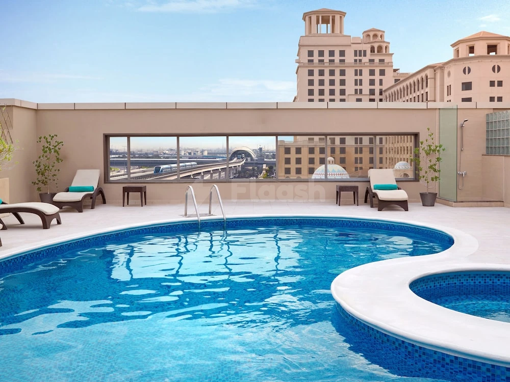 Rooftop pool at Flora Al Barsha Hotel, Dubai, with city views through glass panels and lounge chairs