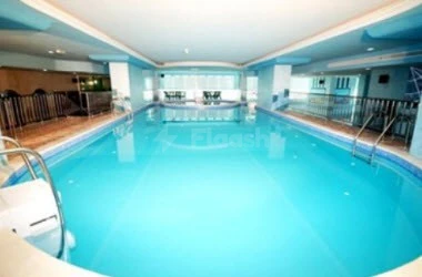 Indoor pool at Al Bustan Tower Hotel Suites, Sharjah, with glass railings and turquoise water