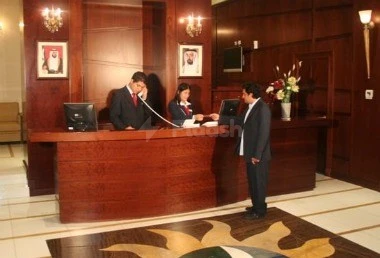 Reception desk at Al Hayat Hotel Apartments, Sharjah, with wooden paneling and framed portraits above counter