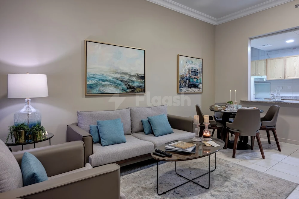 Living room at Al Nakheel Hotel Apartments, Abu Dhabi, featuring coastal artwork and a glass coffee table