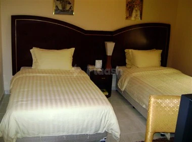 Bedroom at Royal Crown Hotel, Sharjah, featuring twin beds with striped linens and a dark headboard