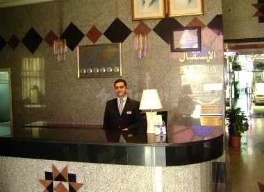 Lobby reception at Royal Crown Hotel, Sharjah, with geometric wall tiles and framed artwork above counter
