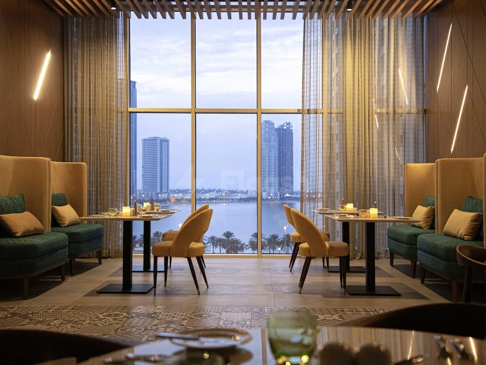 Lounge at Pullman Hotel Sharjah, Sharjah, with teal velvet seating and waterfront city skyline view through floor-to-ceiling