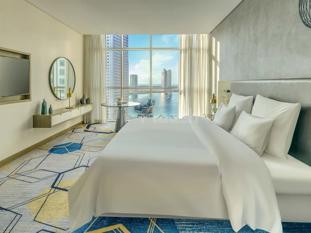 Luxury guest room at Pullman Hotel Sharjah, featuring a king-sized bed and panoramic city views through floor-to-ceiling