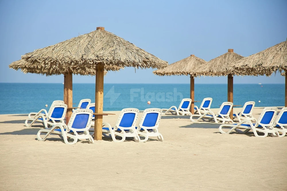 Beach lounge area at Al Hamra Village Hotel, Ras Al Khaimah, with blue chairs under thatched umbrellas facing