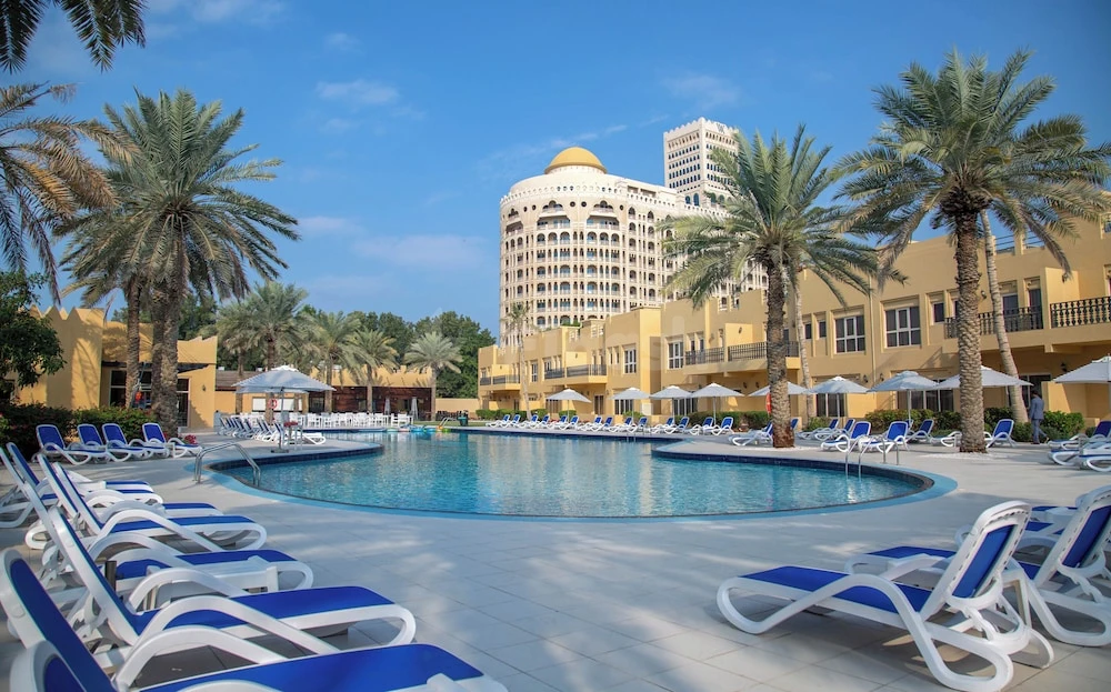 Outdoor pool area at Al Hamra Village Hotel, Ras Al Khaimah, lined with blue lounge chairs and palm