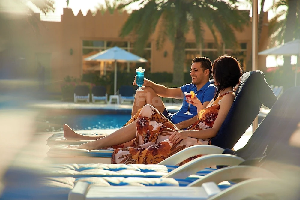 Poolside lounge at Al Hamra Village Hotel, Ras Al Khaimah, with blue-striped sunbeds and palm trees under golden