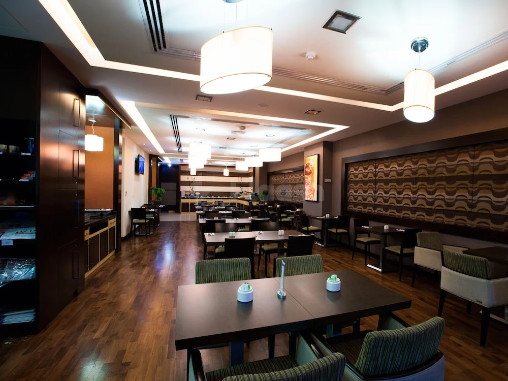 Dining area at Citymax Hotel Sharjah, with dark wood tables, green upholstered chairs, and modern pendant lights